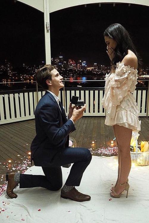 a man kneeling down next to a woman holding a cell phone in front of her